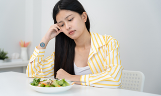 Woman feeling frustrated while staring at a healthy salad, representing diet failure and appetite control challenges.