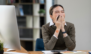 Tired woman at office desk yawning after eight hours of sleep, representing poor sleep quality and daytime exhaustion.