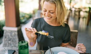 Smiling woman enjoying food at an outdoor café in natural daylight, wearing Patches