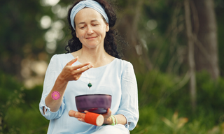 Woman practicing mindfulness outdoors with a singing bowl, representing natural habits that support dopamine, relaxation and mental wellbeing.