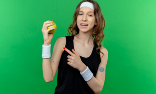 Woman holding a green apple and pointing to a patch on her arm, representing appetite control and healthy weight management.