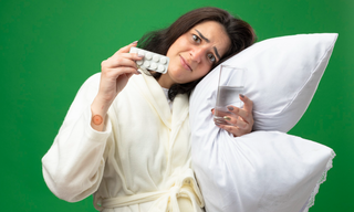 Woman holding melatonin sleep tablets and a glass of water while resting on a pillow, representing sleep support supplements.