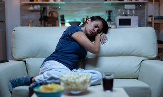Woman resting on a sofa at night with a wellness patch on her arm, representing the connection between sleep, stress, fatigue, and emotional wellbeing.