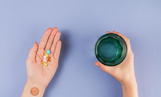 Hand holding colorful pills beside a glass of water, with a wellness patch on the wrist, showing the difference between patches and supplements.