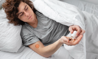 Person lying in bed taking sleeping pills, representing concerns about sleep medication dependence and exploring natural sleep alternatives.