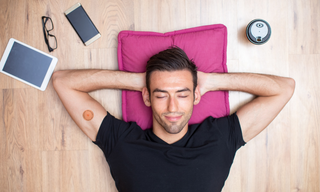 Man relaxing on the floor with eyes closed and hands behind his head, wearing a wellness patch on his arm, showing stress relief and recovery support.