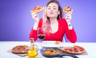 Woman enjoying slices of pizza and comfort food at a table, illustrating food cravings, appetite control, emotional eating, and unhealthy eating habits.