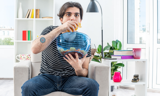 Man snacking from a large bowl while sitting on a couch, representing cravings and emotional eating habits.