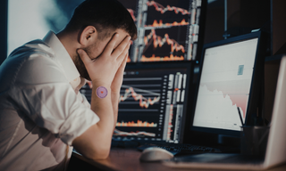 Stressed professional holding his head while working at multiple screens, illustrating chronic stress and mental fatigue.