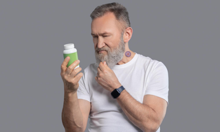Man comparing a supplement bottle while wearing a wellness patch on his neck, illustrating the difference between wellness patches and traditional pills.