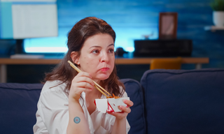 Woman eating takeaway food in the evening at home, representing cravings and hunger when not physically hungry.
