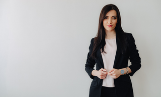 Professional woman in business attire standing confidently while wearing a wellness patch on her wrist.