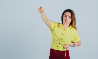 Woman checking waist measurements with a tape measure as part of a weight loss journey.