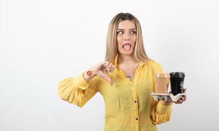 Woman holding takeaway coffee cups and making a disgusted expression, showing dislike for caffeine, with a patch on her arm.