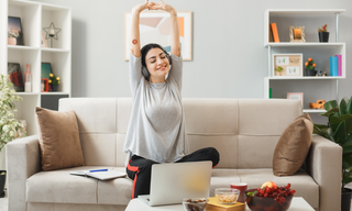 Woman stretching on a sofa while working from home, wearing an energy patch on her arm to support steady afternoon energy and focus.