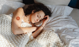 Person sleeping in bed under a blanket with a small support patch on the upper arm, representing nightly sleep support as part of a routine.